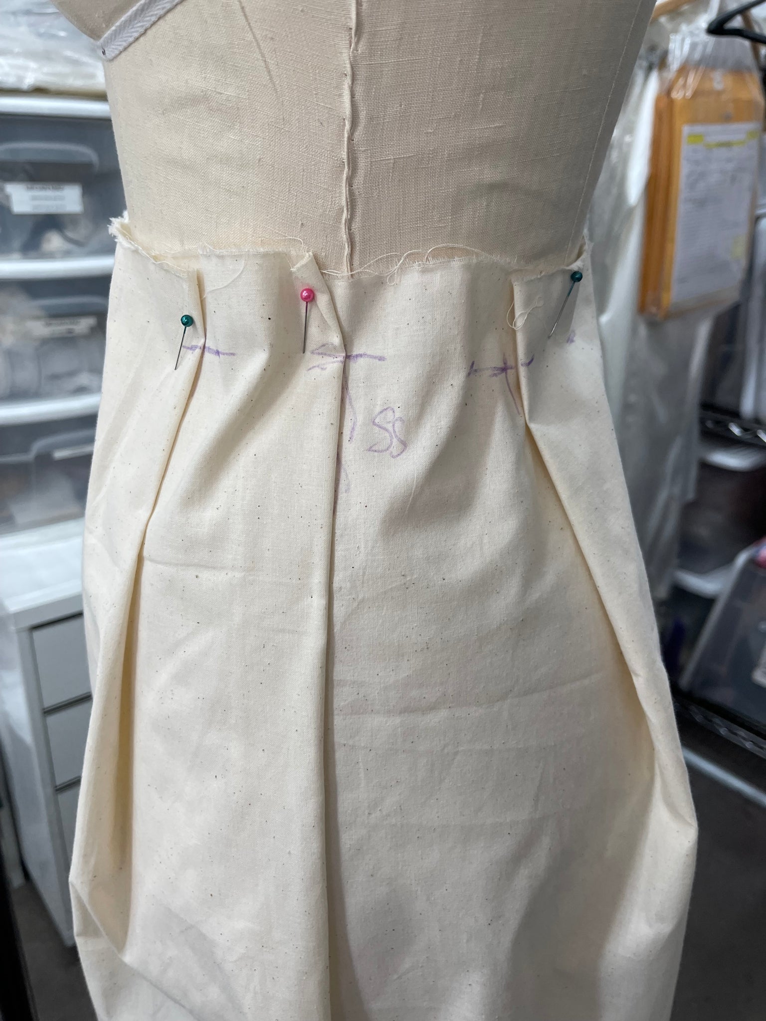 Muslin fabric with sewing lines and pins forming pleats on a mannequin form 